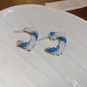 Detailed close-up of C-shaped earrings with blue denim texture and white pearls