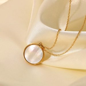Detailed close-up of a 18K gold star and moon shell pendant on cream silk fabric