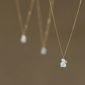 Détail macro du collier en titane doré avec pendentif lapin en nacre blanche polie