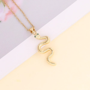 Detailed view of gold snake pendant necklace with green crystal eyes on a book