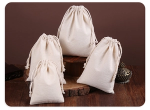 Detail view of four natural cotton canvas drawstring bags on a rustic wood base