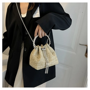 Detail of beige woven straw bucket bag with silver metal handle and fringe tassels