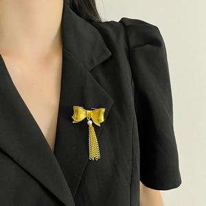 Vintage gold bow brooch with pearls and metal tassels on a minimalist model background