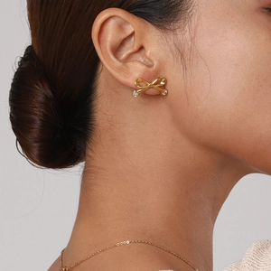 Detail of elegant gold bow earrings with shimmering cubic zirconia on female model