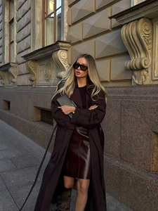 Détail d'un trench-coat marron foncé associé à une jupe en cuir rouge foncé élégante