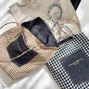 Detailed view of canvas tote bag with denim pocket, gold embroidery and bead straps