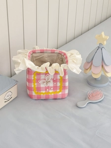 Pink plaid laundry basket with ruffles and pearl butterfly embroidery on a blue surface
