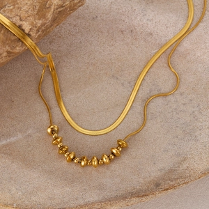 Detail of double-layer gold titanium steel necklace with snake chain and bead accents