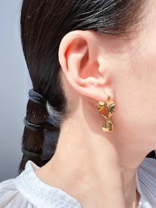 Close-up of golden twisted ribbon earrings with a polished mirror finish on model