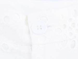 Detailed macro shot of white hollow-out embroidery fabric and matching button