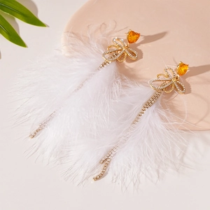 Detailed close-up of white feather earrings with heart-shaped crystal and bow accent