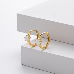 Detailed view of gold plated huggie earrings with round white opal inlay on white background