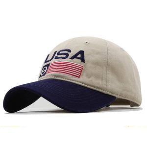 Side view detail of beige baseball cap with navy brim and embroidered USA flag pattern
