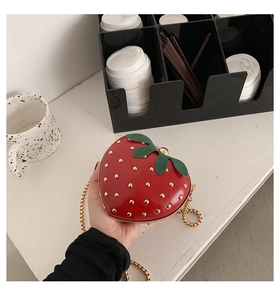 Close-up of strawberry heart-shaped bag with gold studs and delicate metal chain