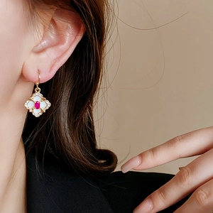 Close-up of a gold four-leaf clover earring with a red gem and small diamonds on model