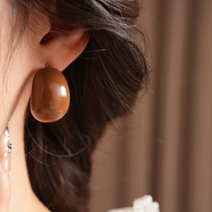 Close-up of model wearing large oval brown resin earrings with a polished glossy finish