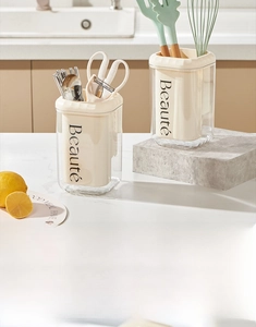 Detail view of cream kitchen utensil holder storing scissors, peeler and whisk on counter
