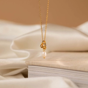 Detail of 18K gold-plated interlocking rings necklace with an elegant white pearl pendant