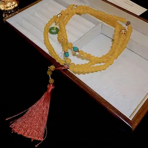 Collier de perles jaunes avec breloque dorée et long gland en soie rouge vif