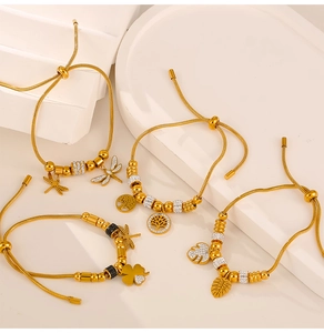 Macro detail of gold snake chain bracelets with sparkling tree of life and leaf charms
