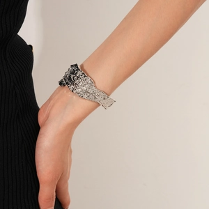 Dettaglio di un bracciale largo in argento con texture lavica irregolare sul polso di una modella