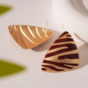 Détail macro de boucles d'oreilles triangulaires dorées avec motif zèbre émaillé