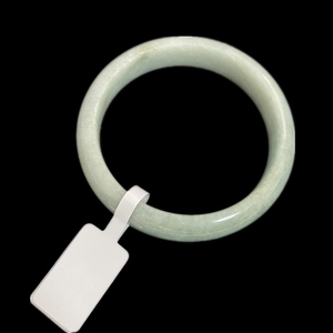 Close-up of a pale green jade bangle with a white adhesive price tag on black background