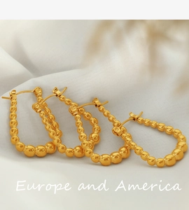 Detailed view of gold geometric earrings with beaded texture on white satin background
