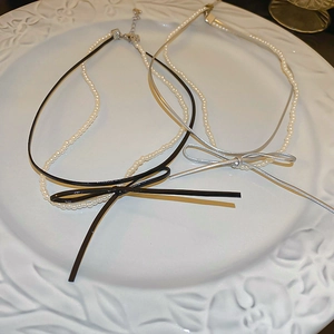 Double-layered faux pearl choker necklace with a sleek black bow in vintage ceramic tray