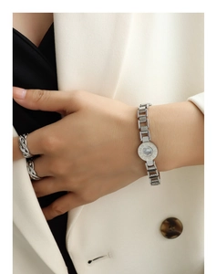 Detailed close-up of silver Roman numeral shell bracelet and twisted ring on wrist