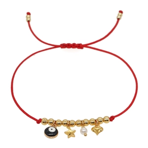 Red string bracelet with gold evil eye, star, heart and pearl charms on white backdrop