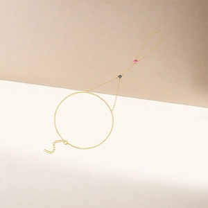 Detail of gold hand chain featuring blue and pink gemstones with adjustable links