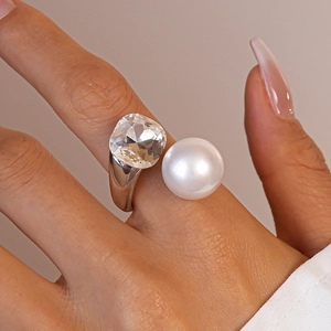 Close-up of a silver ring featuring a large white pearl and transparent cushion-cut crystal