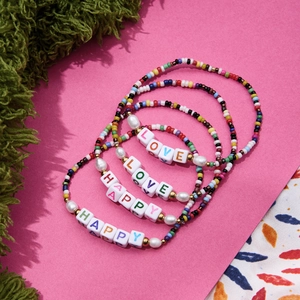 Colorful beaded bracelet set with LOVE and HAPPY letter beads on a bright pink backdrop