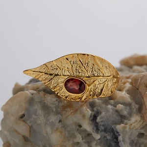 Detailed macro shot of a golden leaf jewelry set featuring a deep red oval garnet gemstone