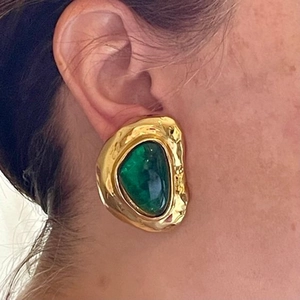 Close-up of a large irregular gold-plated earring with a green resin stone worn by a model