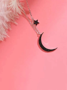 Close-up of moon and star necklace with black zircon inlays on pink background