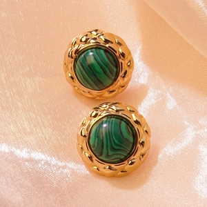 Macro shot of vintage round gold earrings with green malachite stone on satin fabric