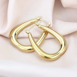 Macro detail of high-polished gold teardrop earrings on elegant pink silk fabric