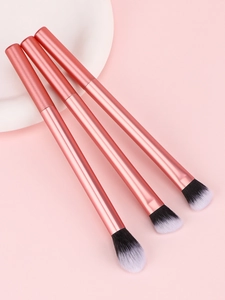Trois pinceaux de maquillage or rose avec poils dégradés sur fond rose doux