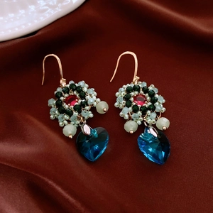 Detailed shot of ethnic beadwork earrings with heart-shaped crystal pendant on silk fabric