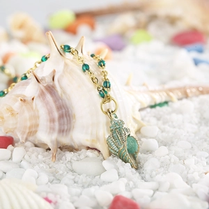 Golden titanium steel necklace with green beads and conch pendant on a beach setting