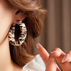 Macro detail of round leopard print earrings with leather texture on female model