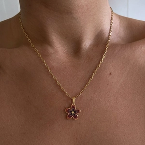 Detailed view of the red enamel flower pendant on a gold plated paperclip chain