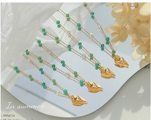 Detail of green crystal bead necklaces with golden tulip pendants on a mirror surface