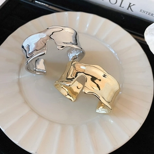 Irregular wide liquid metal open bangle in gold and silver finish on ceramic plate