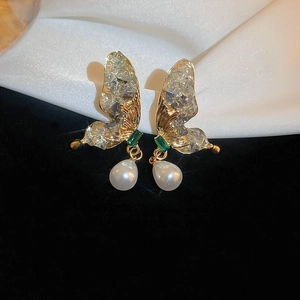Détail de boucles d'oreilles papillon dorées avec pierres vertes et perles sur soie