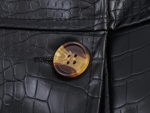 Close-up of a tortoiseshell button on black faux crocodile textured PU leather coat
