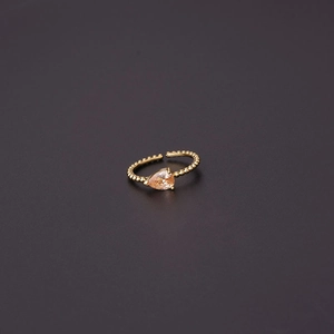 Detailed view of golden teardrop zircon ring with adjustable beaded band on gray background