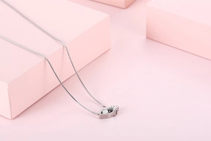 Detailed view of silver stainless steel necklace with hollow eye pendant on pink background